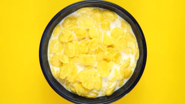 Copos de maíz dorado con leche girando sobre fondo amarillo. Vista superior — Vídeos de Stock
