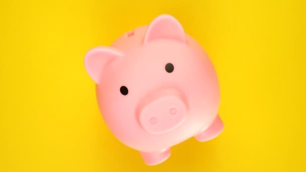 お金の概念を救う。黄色の背景で回転する貯金箱またはペニー銀行. — ストック動画