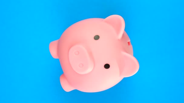 TOP VIEW: Рожевий скарбничка з грошима обертається на синьому фоні — стокове відео