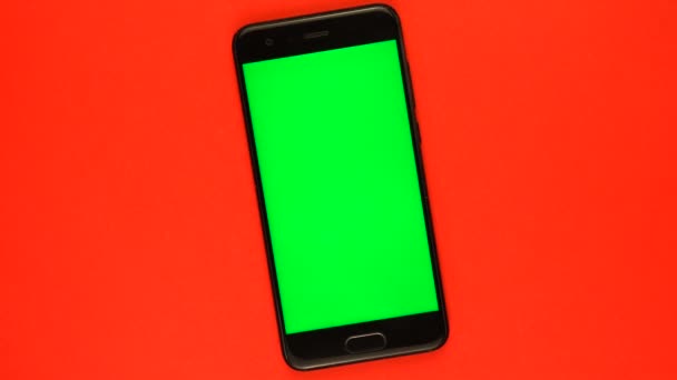 Smartphone negro giratorio lento con pantalla verde sobre fondo rojo. — Vídeo de stock