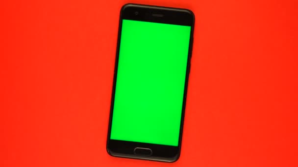 Skutečný smartphone se zelenou obrazovkou otáčí na červeném pozadí. — Stock video