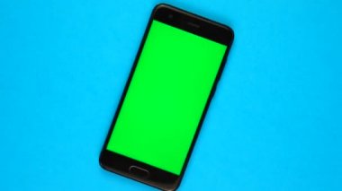 Mavi arka planı olan siyah bir akıllı telefon. Dönüyor. Kolay anahtarlar için yeşil ekran.