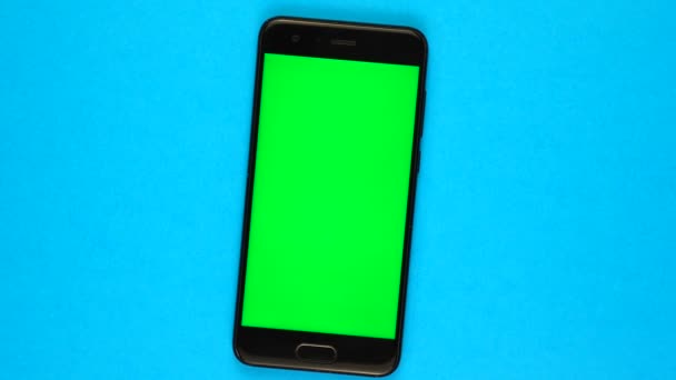Верхний вид: смартфон с зеленым экраном вращается на синем фоне — стоковое видео