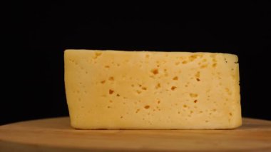 Ahşap tahtada siyah zemin üzerinde delikleri olan sarı peynirin yavaş dönüşü.
