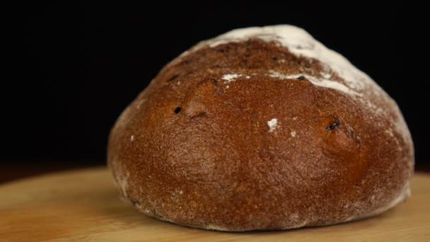 Cały bochenek zakwasionego chleba w zwolnionym tempie na drewnianym stole na czarnym tle — Wideo stockowe