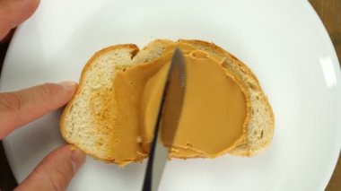 Top view of mans hands spreading peanut butter on wholemeal toast on plate