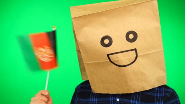 Ritratto di uomo con sacchetto di carta sulla testa sventola bandiera afgana con volto sorridente sullo sfondo verde. — Video Stock