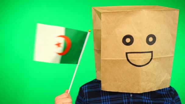 Portrait d'homme avec sac en papier sur la tête agitant drapeau algérien avec visage souriant sur fond vert. — Video