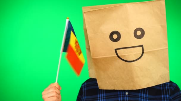 Portret van de mens met papieren zak op hoofd zwaaiend Andorrese vlag met lachend gezicht tegen groene achtergrond. — Stockvideo