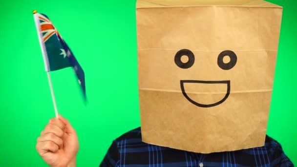 Retrato de hombre con bolsa de papel en la cabeza ondeando bandera australiana con la cara sonriente sobre fondo verde. — Vídeo de stock