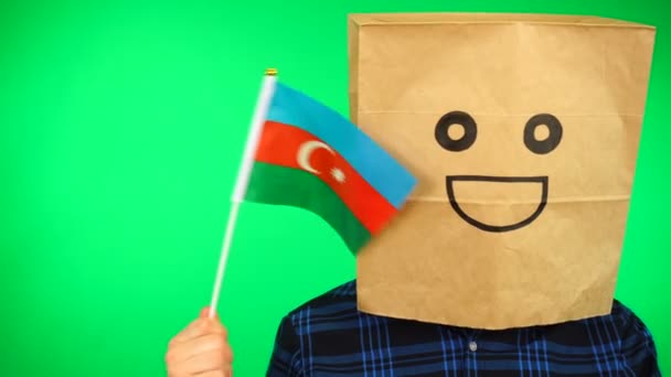 Portrait of man with paper bag on head waving Azerbaijani flag with smiling face against green background. — Stock Video