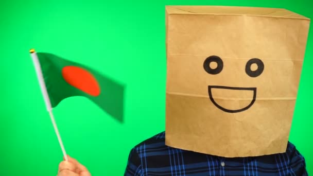 Portrait of man with paper bag on head waving Bangladeshi flag with smiling face against green background. — Stock Video