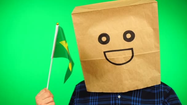 Retrato de hombre con bolsa de papel en la cabeza ondeando bandera brasileña con la cara sonriente sobre fondo verde. — Vídeo de stock