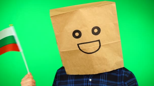 Портрет человека с бумажным пакетом на голове, размахивающим болгарским флагом с улыбающимся лицом на зеленом фоне. — стоковое видео