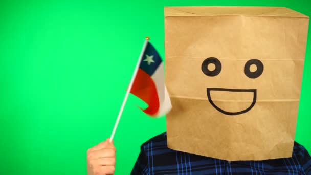 Retrato de hombre con bolsa de papel en la cabeza ondeando bandera chilena con la cara sonriente sobre fondo verde. — Vídeo de stock