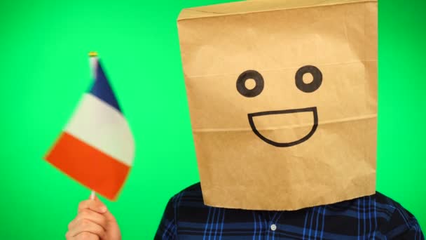 Ritratto di uomo con sacchetto di carta sulla testa sventola bandiera francese con volto sorridente sullo sfondo verde. — Video Stock