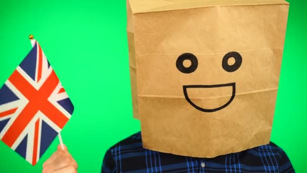 Portrait of man with paper bag on head waving Union Jack flag with smiling face against green background. — Stock Video