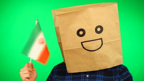 Portret mężczyzny z papierową torbą na głowie machającego irańską flagą z uśmiechniętą twarzą na zielonym tle. — Wideo stockowe