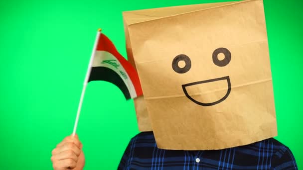 Portret mężczyzny z papierową torbą na głowie machającego iracką flagą z uśmiechniętą twarzą na zielonym tle. — Wideo stockowe