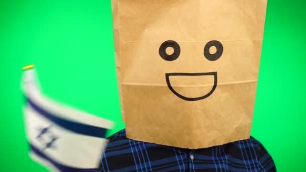 Ritratto di uomo con sacchetto di carta sulla testa sventola bandiera ebraica con volto sorridente sullo sfondo verde. — Video Stock