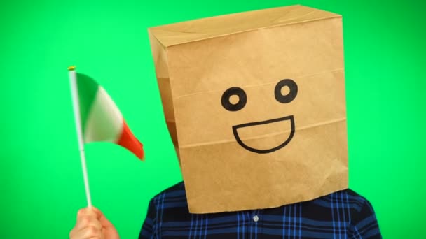 Portrait of man with paper bag on head waving Italian flag with smiling face against green background. — Stock Video