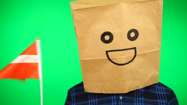 Portret mężczyzny z papierową torbą na głowie machającego łotewską flagą z uśmiechniętą twarzą na zielonym tle. — Wideo stockowe