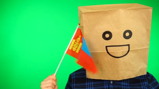 Portret van de mens met papieren zak op het hoofd zwaaiend Mongoolse vlag met glimlachend gezicht tegen groene achtergrond. — Stockvideo