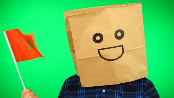 Портрет человека с бумажным пакетом на голове, размахивающим марокканским флагом с улыбающимся лицом на зеленом фоне. — стоковое видео