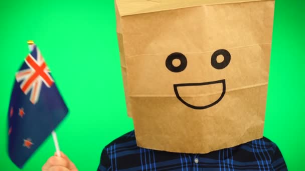 Portrait of man with paper bag on head waving New zealand flag with smiling face against green background. — Stock Video