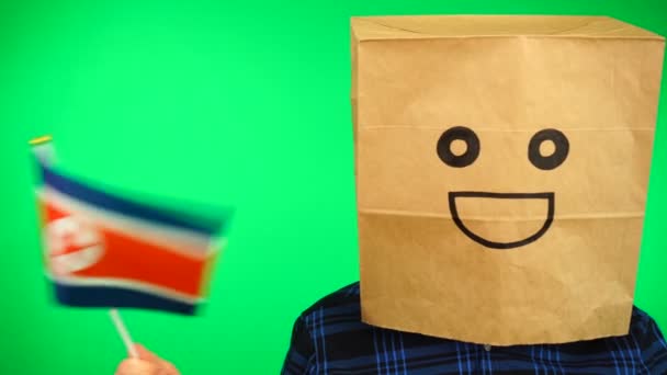 Portrait of man with paper bag on head waving North Korean flag with smiling face against green background. — Stock Video
