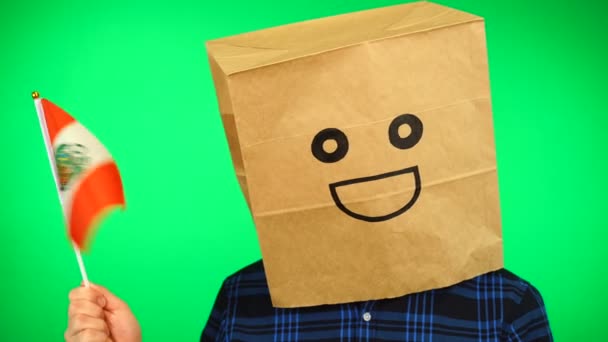 Портрет человека с бумажным пакетом на голове, размахивающим перуанским флагом с улыбающимся лицом на зеленом фоне. — стоковое видео
