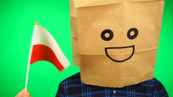 Kafasında kese kağıdı olan, yeşil arka planda gülümseyen Polonya bayrağı sallayan bir adam portresi.. — Stok video