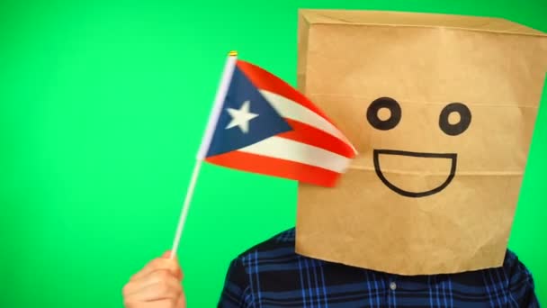 Porträtt av man med papperspåse på huvudet viftar Puerto Ricas flagga med leende ansikte mot grön bakgrund. — Stockvideo