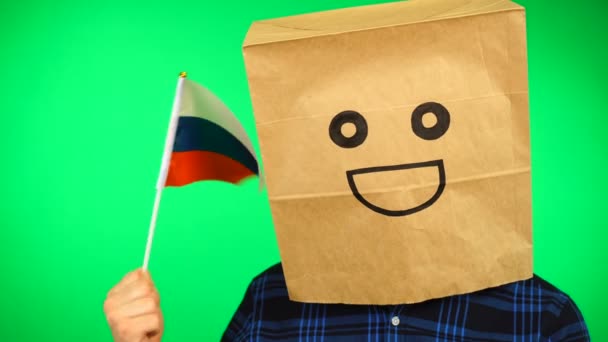 Portrait of man with paper bag on head waving Russian flag with smiling face against green background. — Stock Video