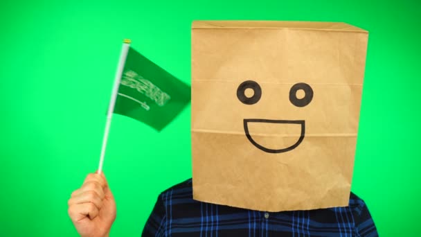 Retrato de hombre con bolsa de papel en la cabeza ondeando bandera saudí con la cara sonriente contra el fondo verde. — Vídeo de stock