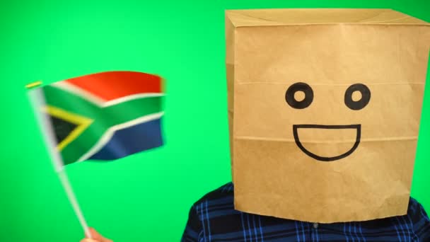 Kafasında kağıt torba olan ve yeşil arka planda gülümseyen Güney Afrika bayrağı sallayan bir adamın portresi.. — Stok video