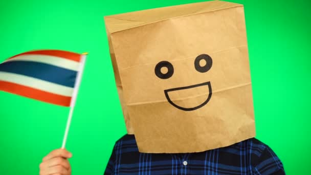 Portrait of man with paper bag on head waving Thai flag with smiling face against green background. — Stock Video