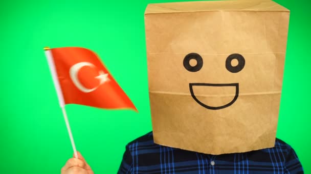 Porträtt av man med papperspåse på huvudet viftande turkisk flagga med leende ansikte mot grön bakgrund. — Stockvideo