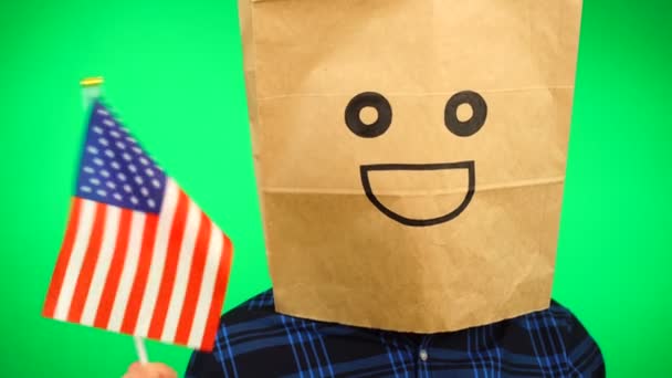 Portrét muže s papírovým sáčkem na hlavě mávající americkou vlajkou s usmívající se tváří na zeleném pozadí. — Stock video