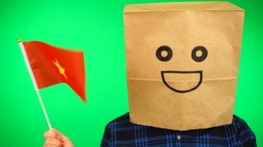 Kafasında kağıt torba olan, yeşil arka planda gülümseyen yüzü olan Vietnam bayrağı sallayan bir adam portresi..