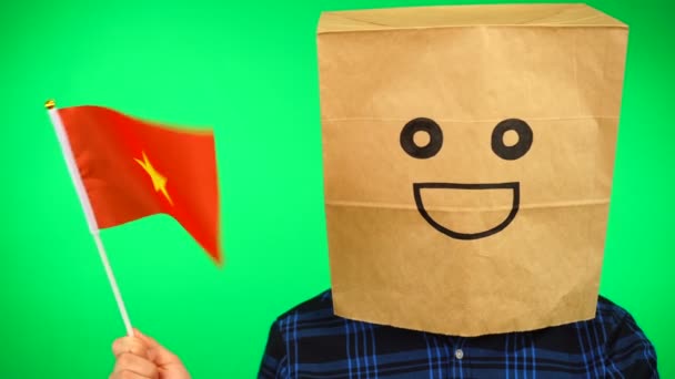 Retrato de homem com saco de papel na cabeça acenando bandeira vietnamita com rosto sorridente contra fundo verde. — Vídeo de Stock