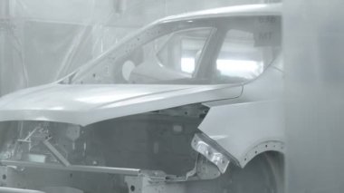 Koşu bandındaki araç parçalarını boyamak. Araba üretim fabrikası. Boyacı çarpışan bir arabaya beyaz boya püskürtür..