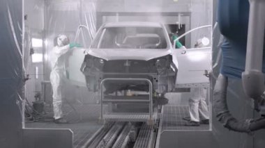 Koşu bandındaki araç parçalarını boyamak. Araba üretim fabrikası. İki ressam çarpışan bir arabaya beyaz boya sıkarlar..