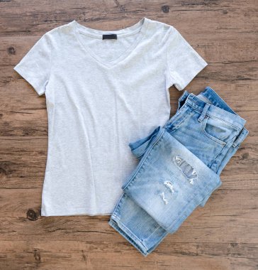 Grey T-shirt and jeans mock up flat lay on wooden background. Top front view