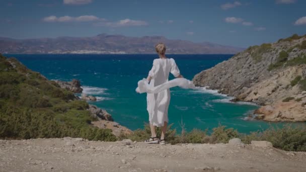 一个穿着白衣的年轻貌美的女人，背靠着美丽的海景. — 图库视频影像