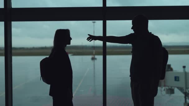 Ένα ζευγάρι στο αεροδρόμιο περιμένει για μια πτήση. Μια γυναίκα και ένας άντρας επικοινωνούν στο βάθος του παραθύρου.. — Αρχείο Βίντεο