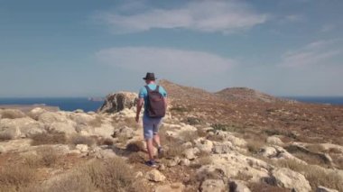Sırt çantalı bir turist deniz kenarındaki vahşi bir arazide ve bir uçurumda yürüyor..