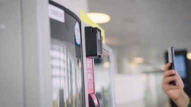 Çerçevede akıllı telefonu ve otomatı olan bir adam eli var. Adam kahvesini ve abur cuburunu ödüyor..