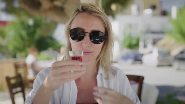 Mujer joven en la veranda de verano del restaurante, bebiendo tintura roja — Vídeos de Stock