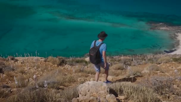 Um cara, um turista com uma mochila, desce a encosta para o belo mar Mediterrâneo. — Vídeo de Stock